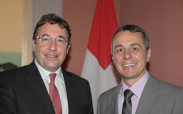 Ignazio Cassis e Achim Steiner in piedi davanti alla bandiera svizzera.