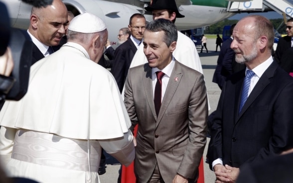 The Pope shakes Ignazio Cassis' hand in front of an Alitalia plane. President Berset and National Council President de Buman are standing next to him.