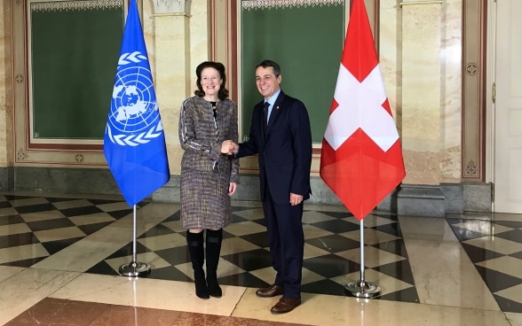 Federal Councillor Cassis shakes hands with Henrietta Fore. In the background the flags of Switzerland and the UN can be seen. 