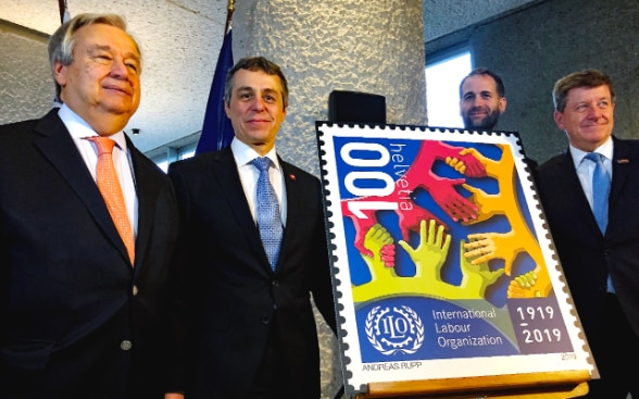 Federal Councillor Cassis and UN Secretary-General António Guterres are standing next to a special stamp commemorating the 100th anniversary of the ILO.