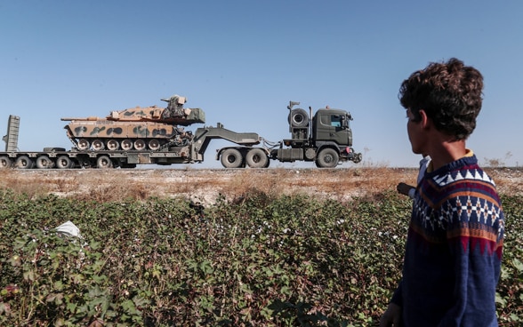 Un lavoratore in un campo di cotone della regione di Sanliurfa osserva il passagio di un convoglio militare turco diretto nel nord-est della Siria