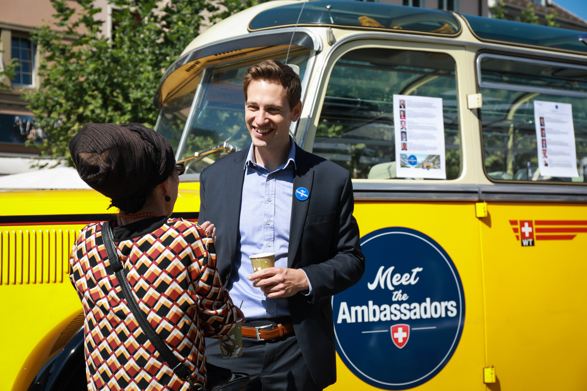 An ambassador talks to a visitor; in the background is the bus Meet the Ambassador