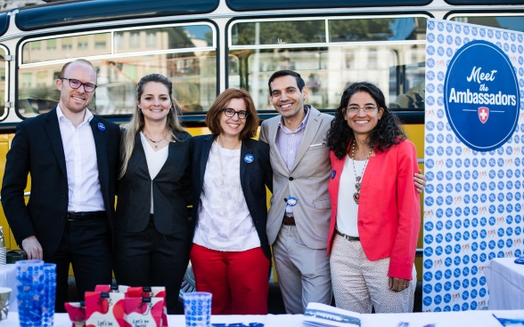 A group of five ambassadors pose in front of the yellow bus for the photo