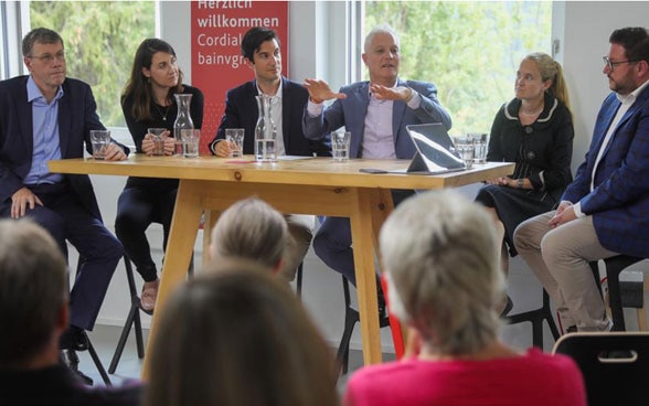 Schweizer Botschafterinnen und Botschafter sitzen bei ihrem Besuch in der Bündner Gemeinde Scuol um einen Tisch und diskutieren mit dem Publikum über die Schweizer Aussenpolitik und ihre Arbeit.