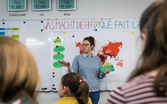 Kinder hören einer Frau zu, welche die Arbeit der Humanitären Hilfe der Schweiz präsentiert.