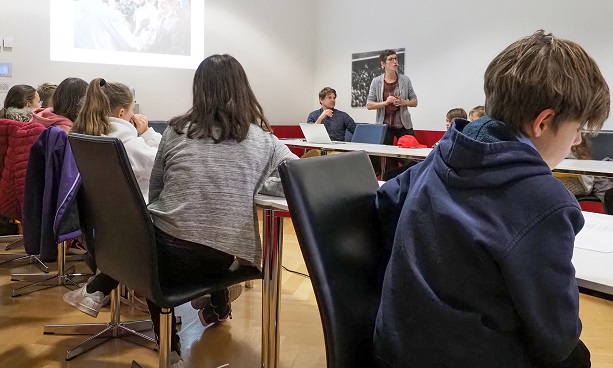 : Kinder hören einer Frau zu, welche die Arbeit der Kommunikationsabteilung des EDA präsentiert.