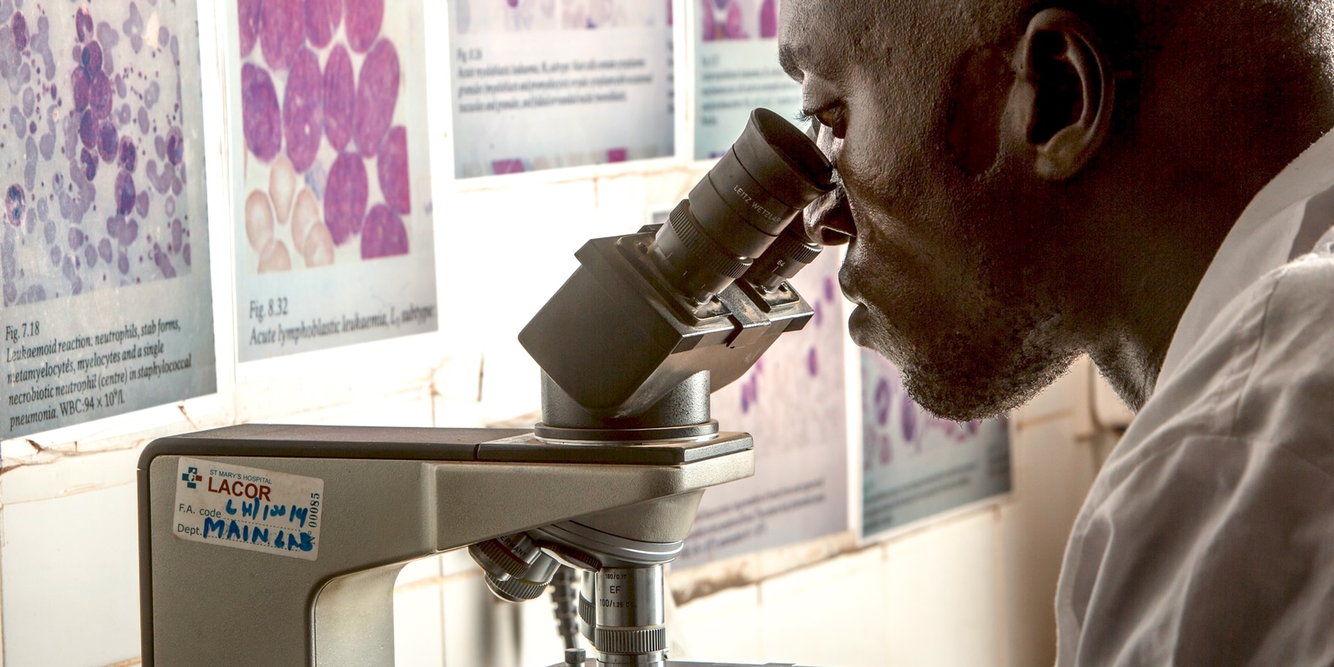 Ein Mitarbeiter in einem Spital blickt durch ein Mikroskop.