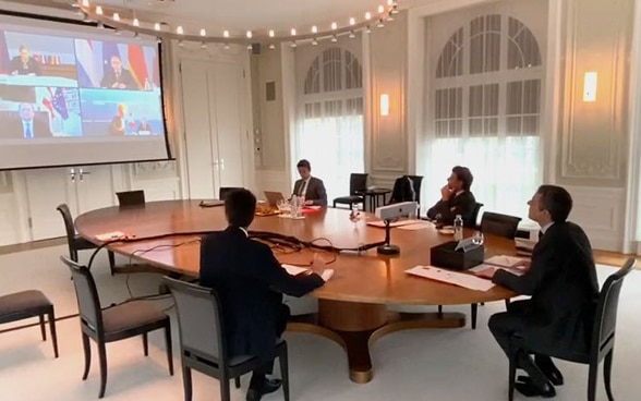 Bundesrat Ignazio Cassis sitzt an einem Tisch: Vor ihm ein Bildschirm, auf dem die Aussenminister von Deutschland, Österreich, Liechtenstein und Luxemburg zu sehen sind.