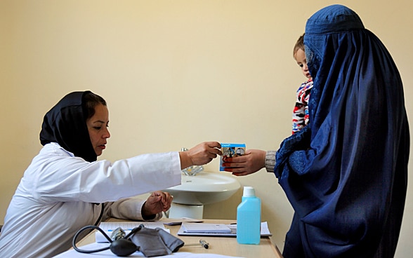 Une doctoresse tend une boîte de médicaments à une femme qui porte un enfant dans les bras.