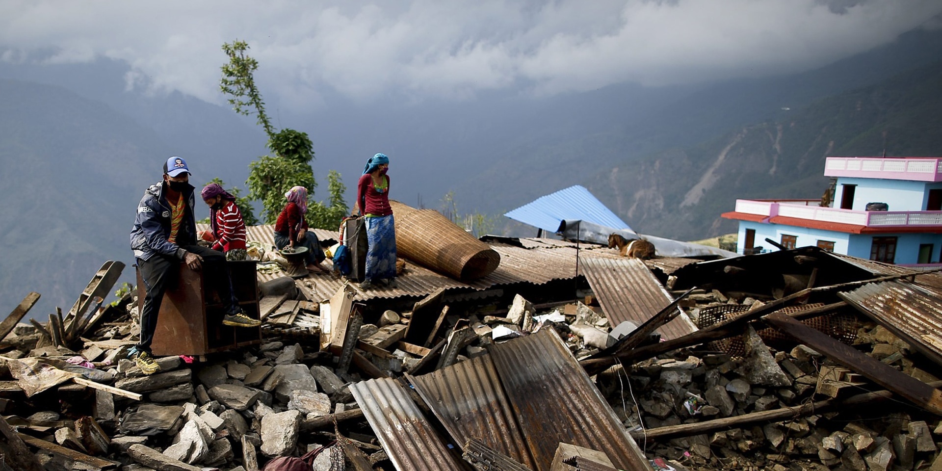 Eine nepalesische Familie mit zwei Kindern sitzt auf den Trümmern ihres Hauses in einem Dorf in den Bergen.