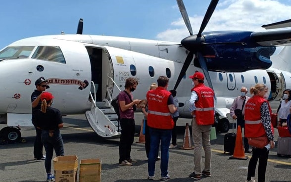 Passeggeri e membri dell'Ambasciata svizzera davanti a un velivolo, sulla pista dell’aeroporto.