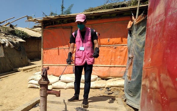 Un homme vêtu d’un gilet rose désinfecte un puits dans un camp de réfugiés au Bangladesh. 