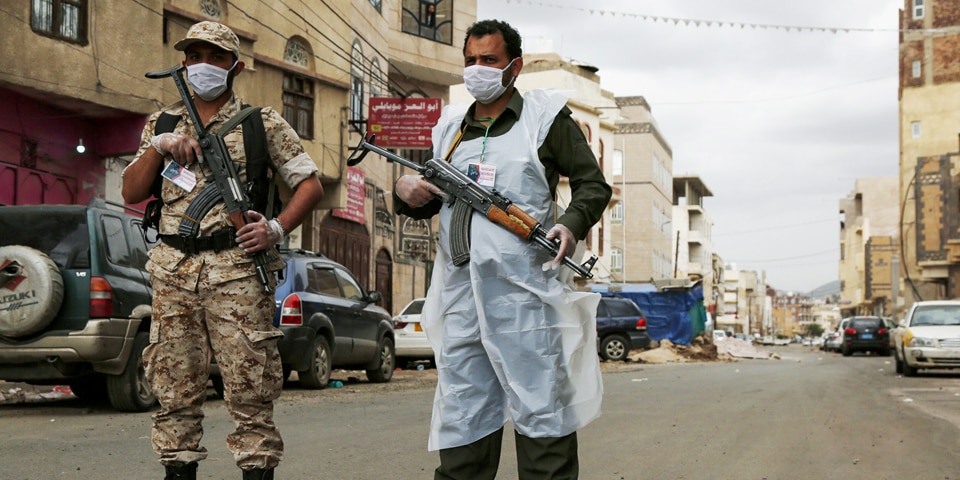 Two armed soldiers are checking a street. Both soldiers are wearing firearms and facial masks, one is wearing sanitary clothes.