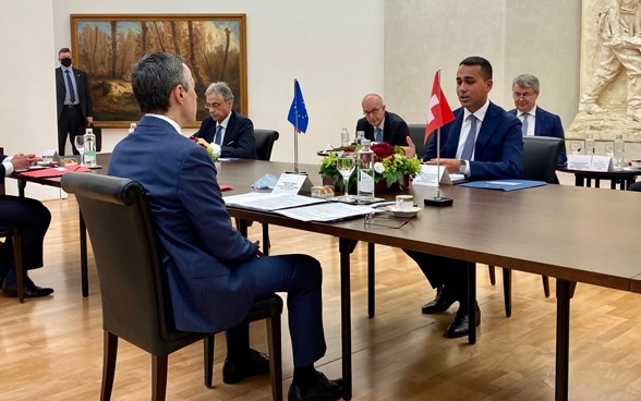 Federal Councillor Cassis and the Italian Foreign Minister Luigi Di Maio sit at a wooden table and hold a conversation.