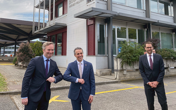 Bundesrat Ignazio Cassis und Staatssekretär Lemoyne berühren sich mit dem Ellbogen. Rechts daneben steht der Genfer Staatsratspräsident Antonio Hodgers. 