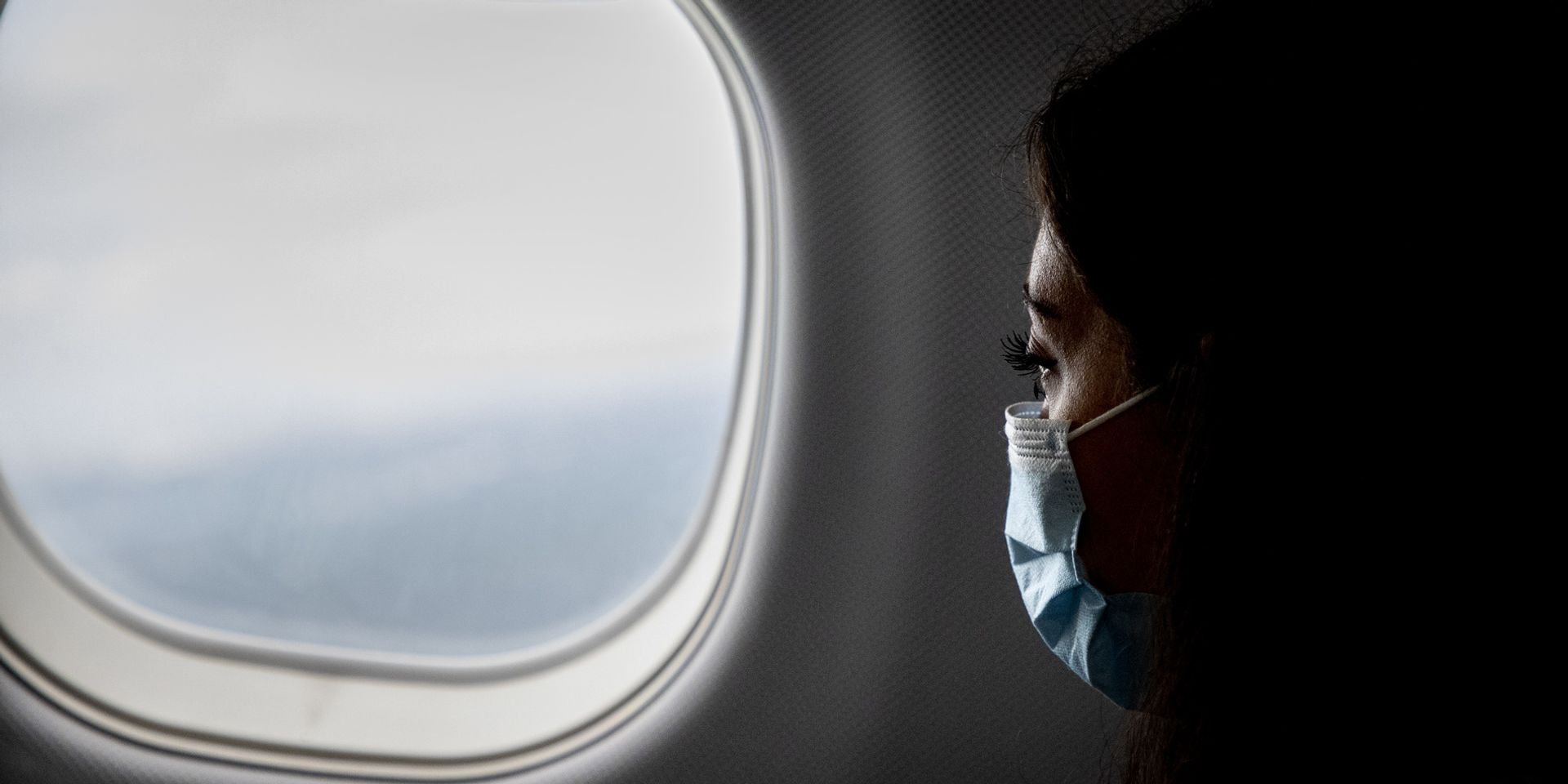 Eine Frau mit Gesichtsmaske schaut aus dem Flugzeugfenster.
