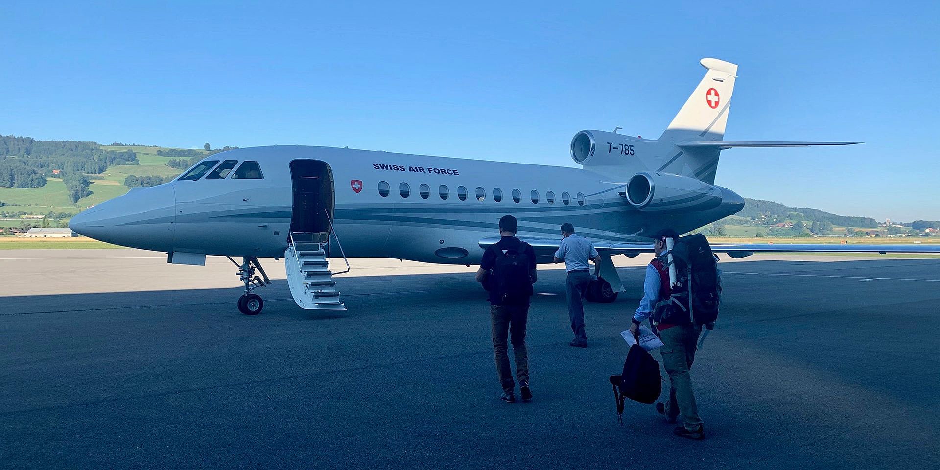 Drei Personen gehen zu einem Flugzeug, das auf dem Rollfeld steht. 