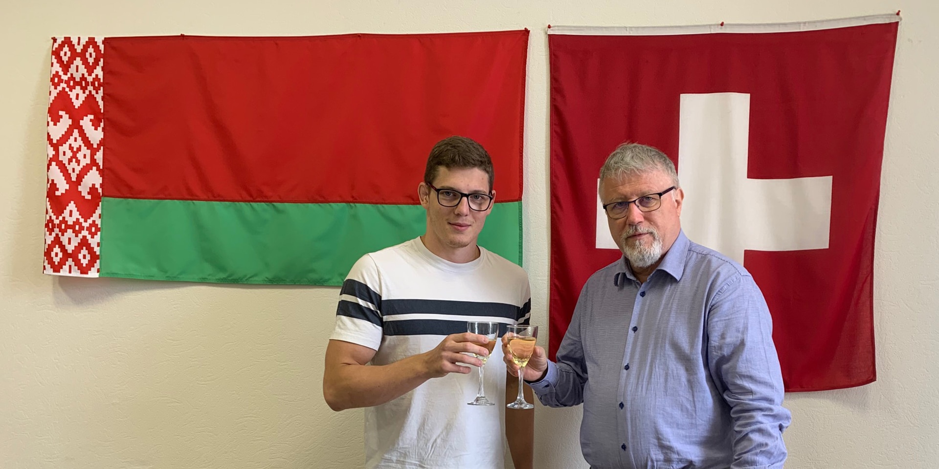 Zwei Männer stehen vor einer Wand mit den Flaggen von Belarus und der Schweiz. 