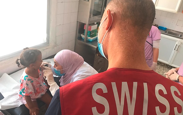 Une petite fille est examinée par le personnel médical local, assisté par un expert de l’unité médicale mère-enfant.
