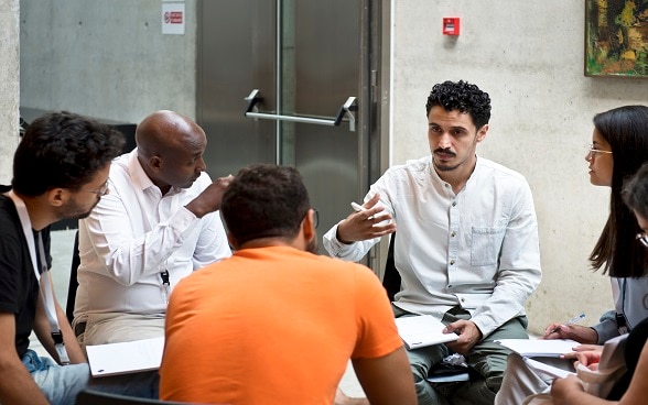 A group of young people, sitting in a circle, talk and share experiences from their respective countries.