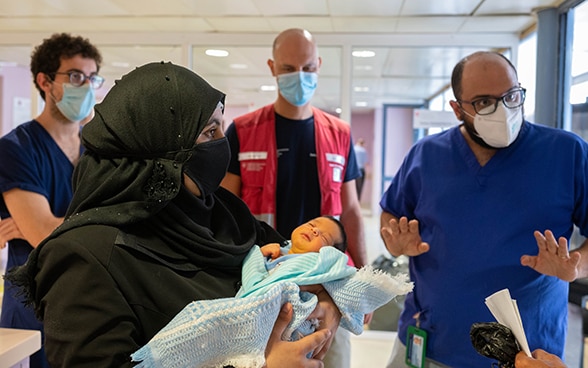 A woman holding a newborn baby in her arms talks to specialists. 