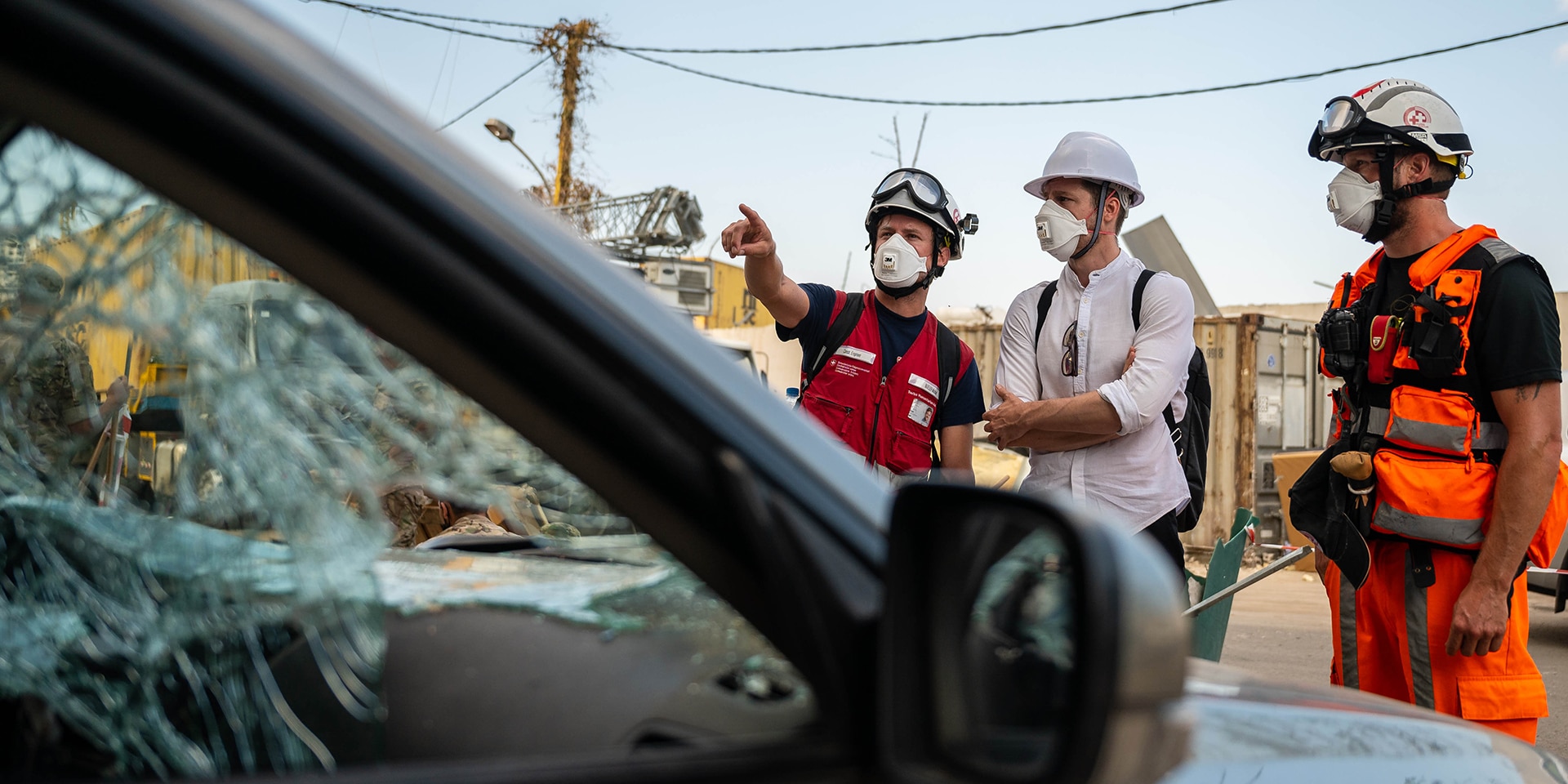 Drei Experten der Humanitären Hilfe des Bundes stehen bei einem kaputten Auto.