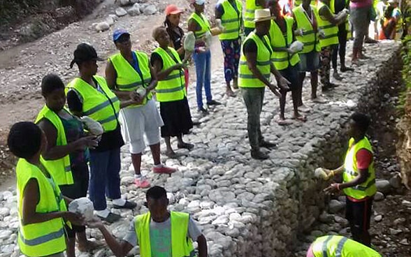 Several people wearing yellow safety waistcoats are building new gabions with stones.