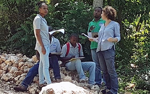 Constance Jaillet, in piedi con dei fogli in mano, parla con quattro persone del luogo.