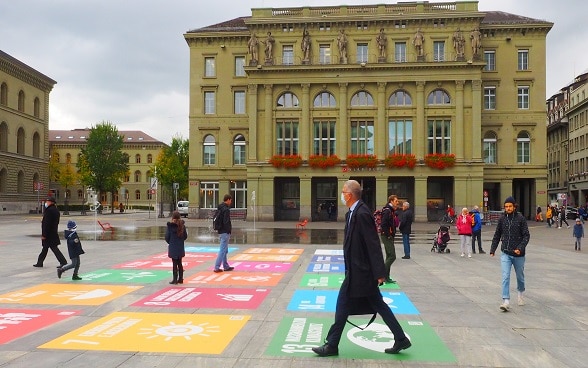 Des passants regardent le Palais fédéral sur lequel s’affichent des images évoquant les 17 objectifs de développement durable de l’Agenda 2030.