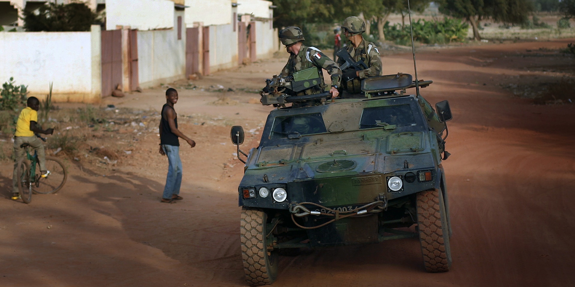 Military vehicle drives over a sand road of a village.