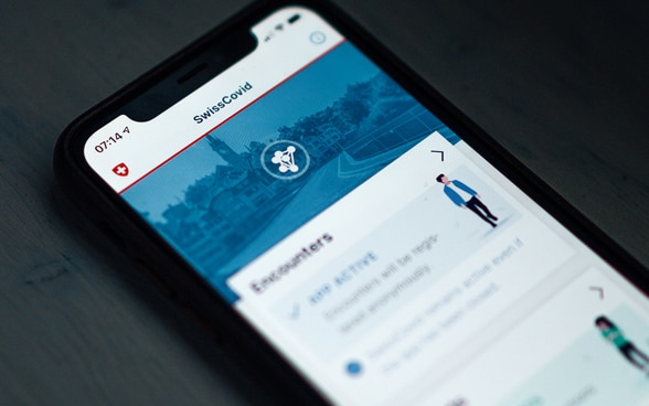 A smartphone on a table showing the homepage of the SwissCovid application.