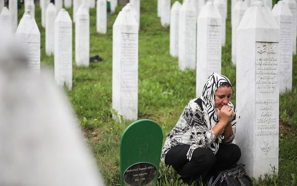 A woman kneels beside a memorial stone at the cemetery in Srebrenica.