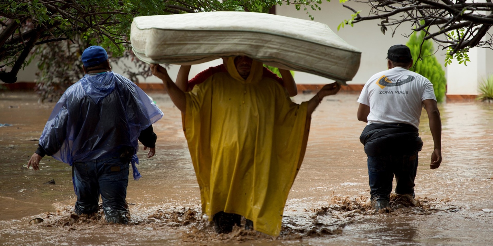 Two people carrying a mattress through the floods, accompanied by two aid workers. 
