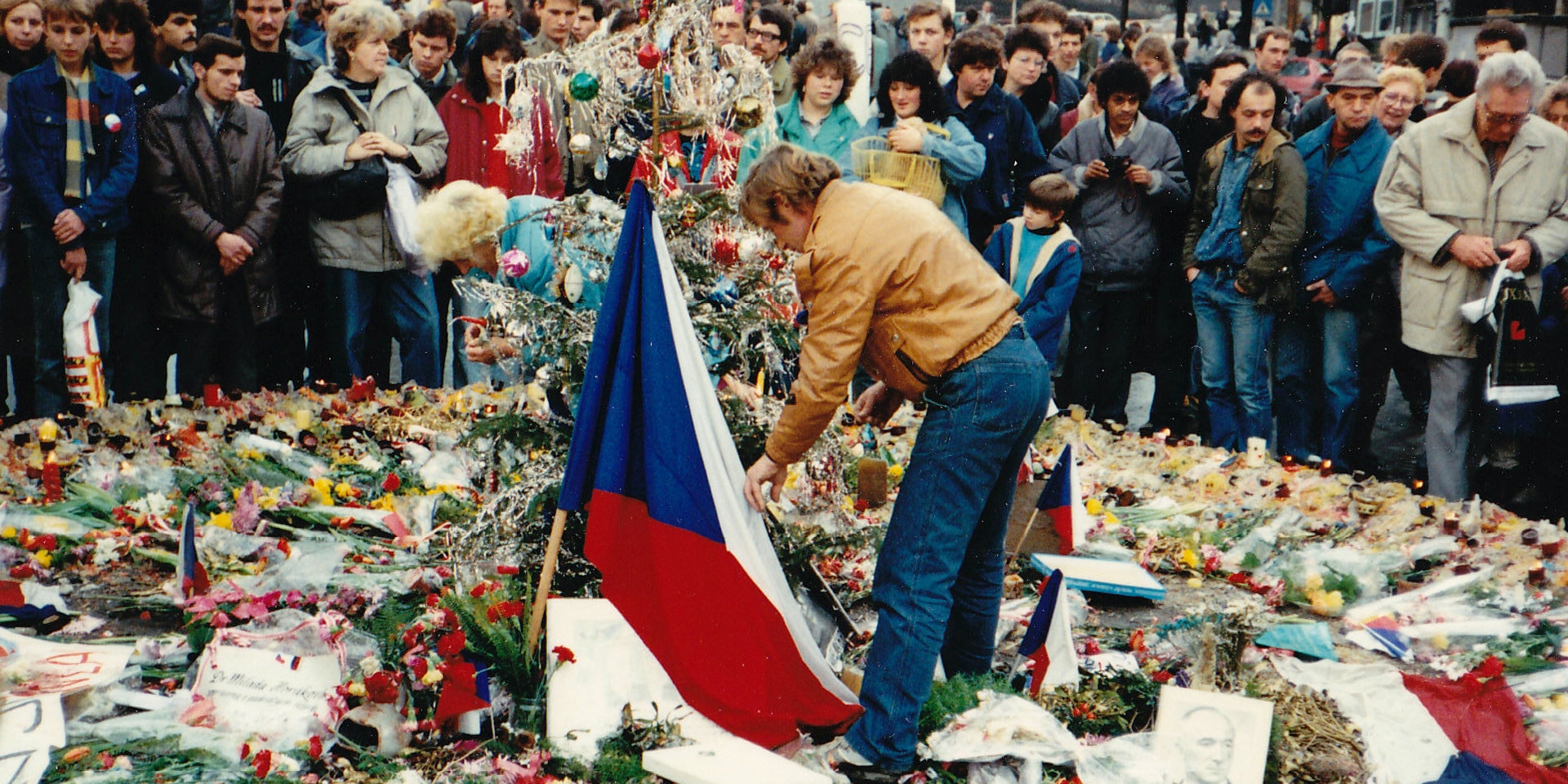 Václav Havel depone dei fiori in piazza San Venceslao circondato da un gruppo di persone.