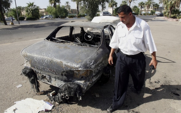 An Iraqi policeman inspects a burnt-out car.