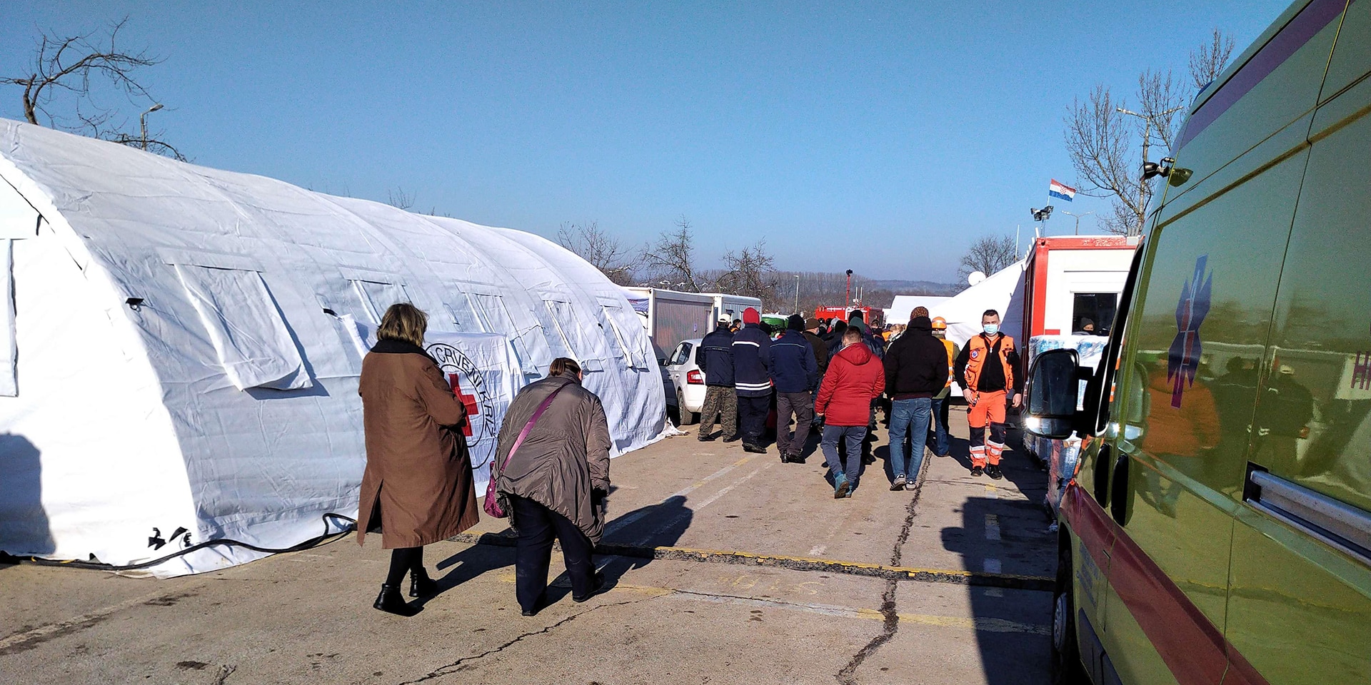 A white tent, an ambulance and other vehicles belonging to the civil protection authorities and humanitarian organisations. People working to provide assistance.