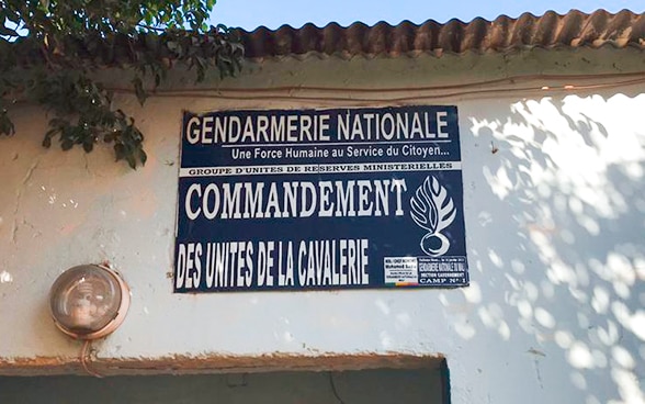 La façade de l’unité de cavalerie de la gendarmerie nationale malienne. Une panccarte bleue est accolée sur un mur blanc.