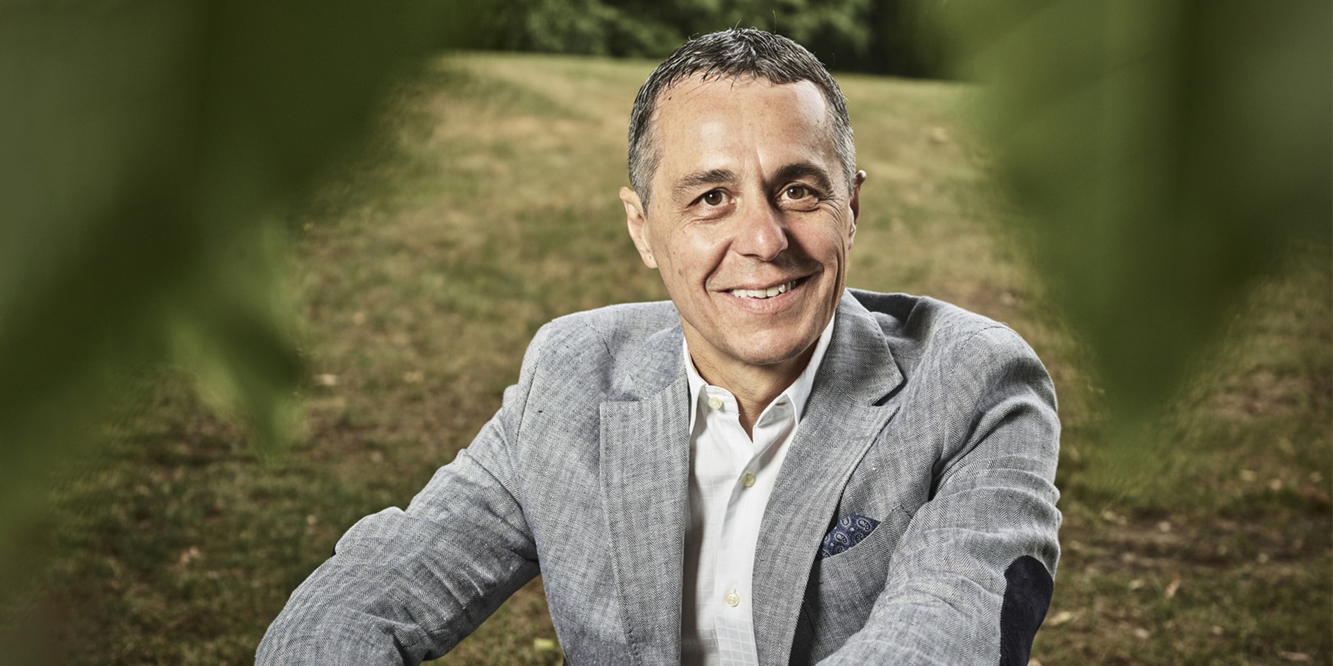 Portrait of Federal Councillor Ignazio Cassis sitting in a meadow. 