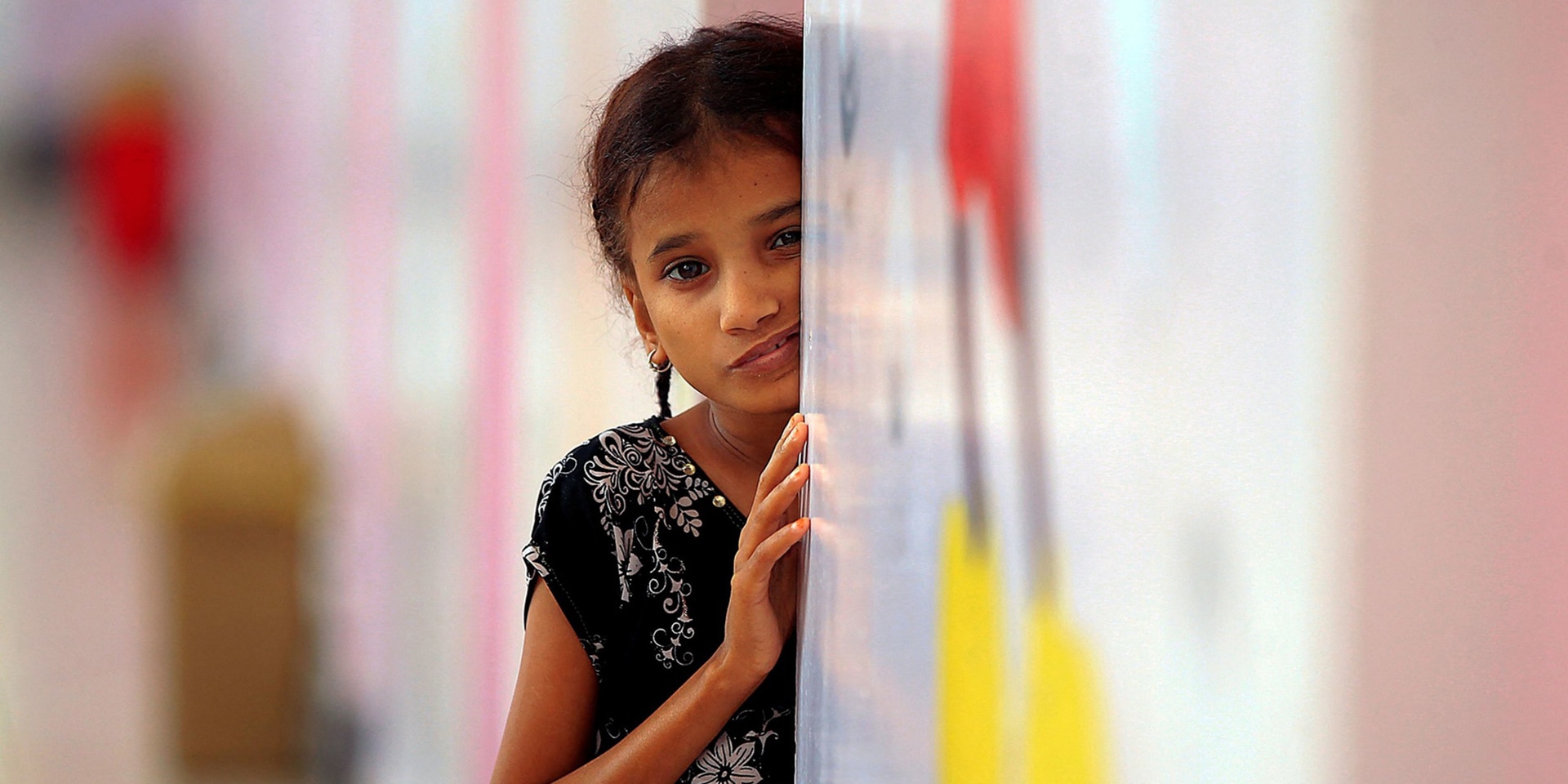 Une petite fille, le regard inquiet, est appuyée à un mur attendant de recevoir à manger.