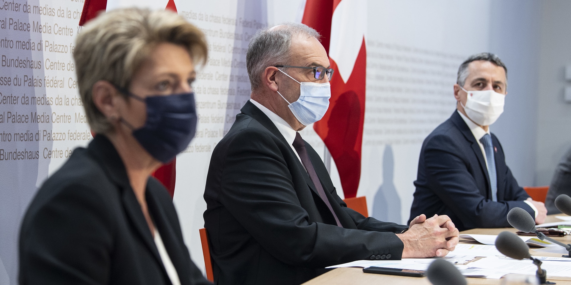 Bundespräsident Guy Parmelin, Bundesrat Cassis und Bundesrätin Karin Keller-Sutter sitzen auf dem Podium des Medienzentrums in Bern.