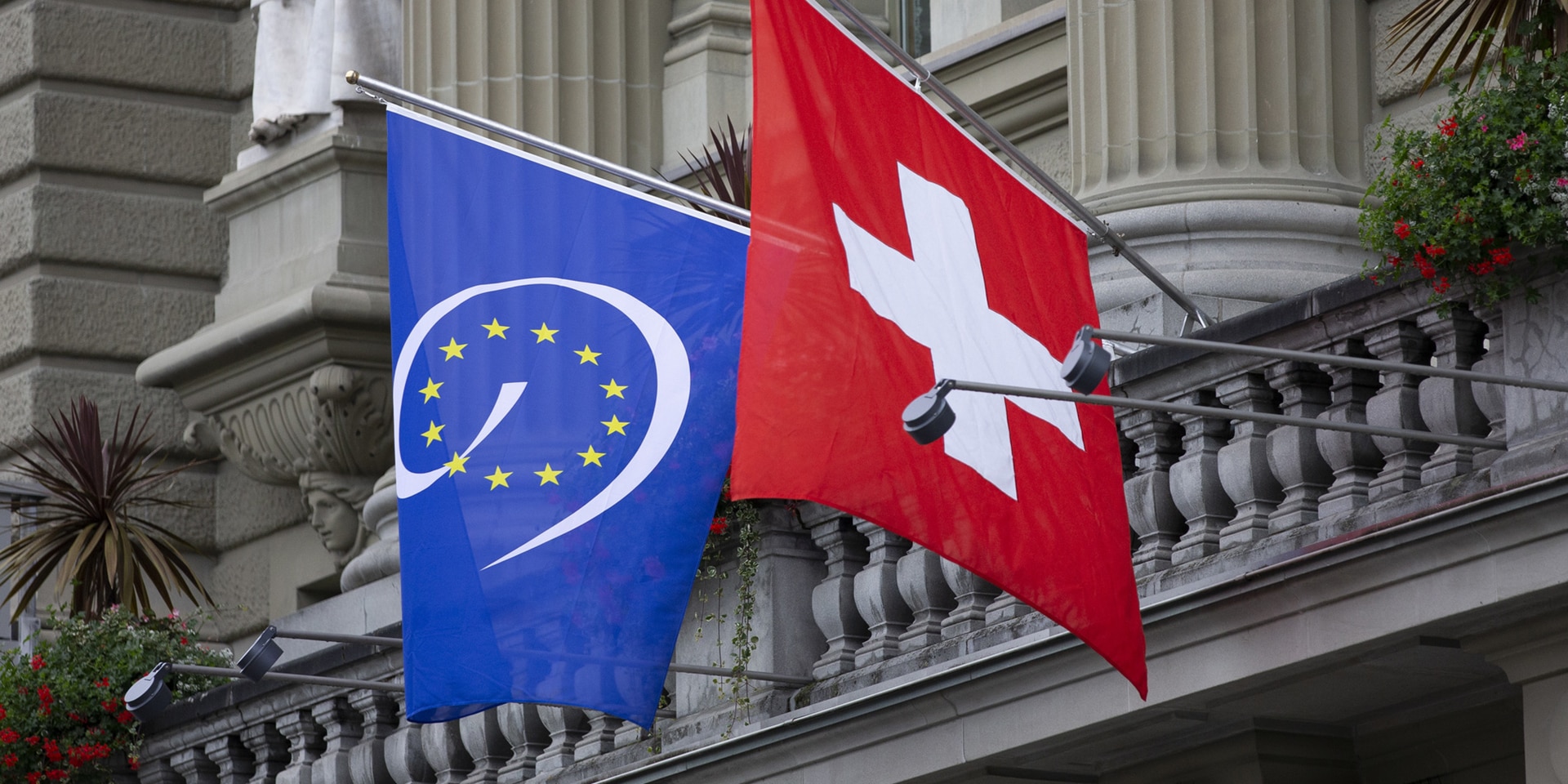 The national flag of Switzerland and the flag of the Council of Europe hanging on the Federal building.