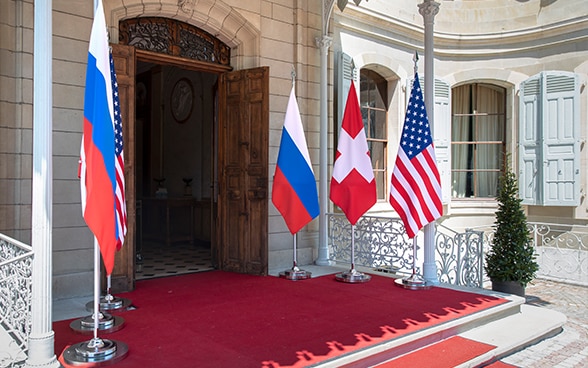 Vue de l'entrée de la Villa La Grange ornée d’un tapis rouge devant la porte et flanquée des drapeaux suisse, américain et russe.