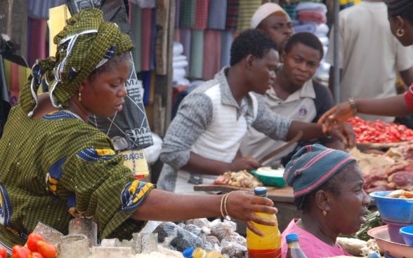 In un mercato in Africa una donna prende in mano una bottiglia per venderla.