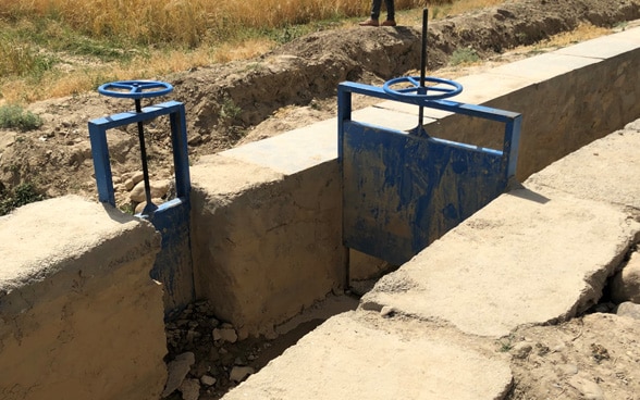 Ein Bewässerungskanal mit einer blauen Schleuse in einer kargen Region Afghanistans. 