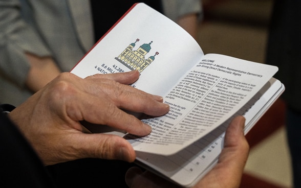 Federal Councillor Ignazio Cassis looks through the small book. His hands opening the book are in the foreground.