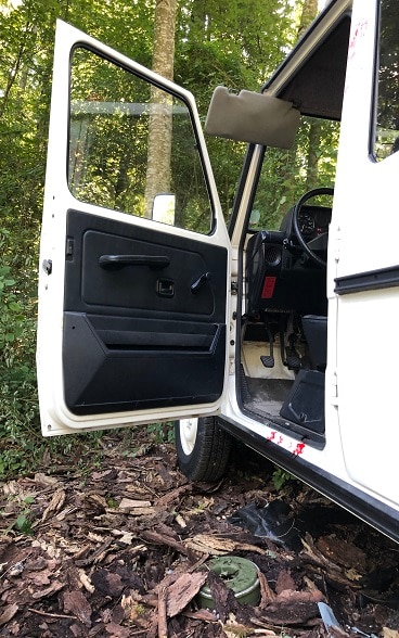 A green mine lying on the ground next to the open door of a white jeep