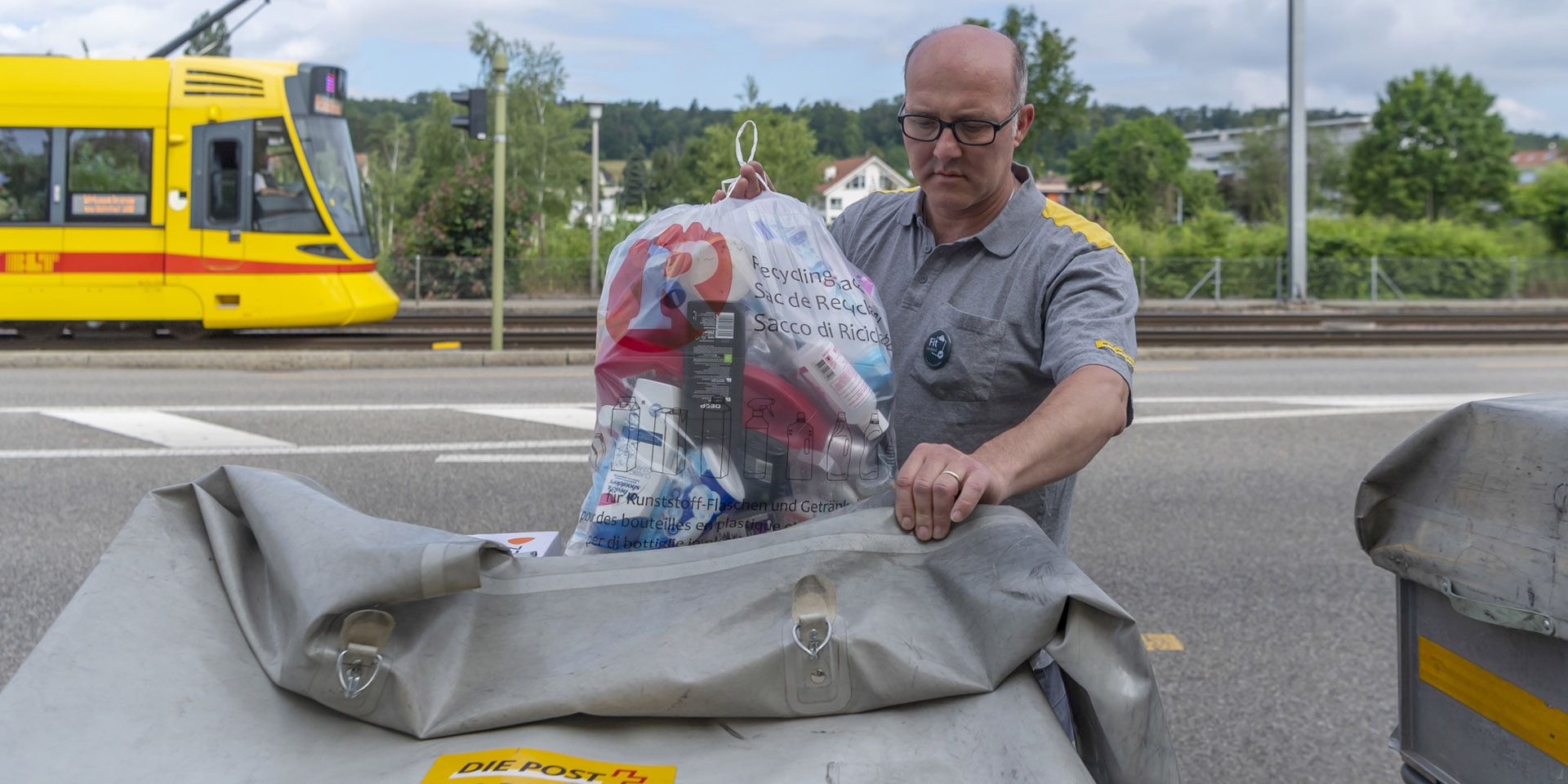 A postman puts a recycling bag with empty plastic bottles and drink cartons in his wagon. 
