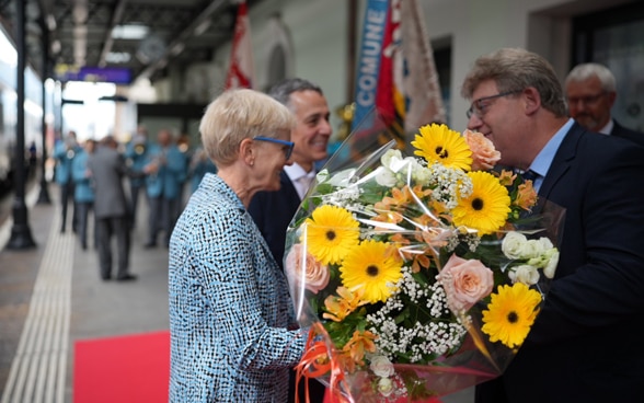 Sul binario della stazione ferroviaria di Biasca, Paola Cassis riceve un mazzo di fiori da parte del Sindaco. 