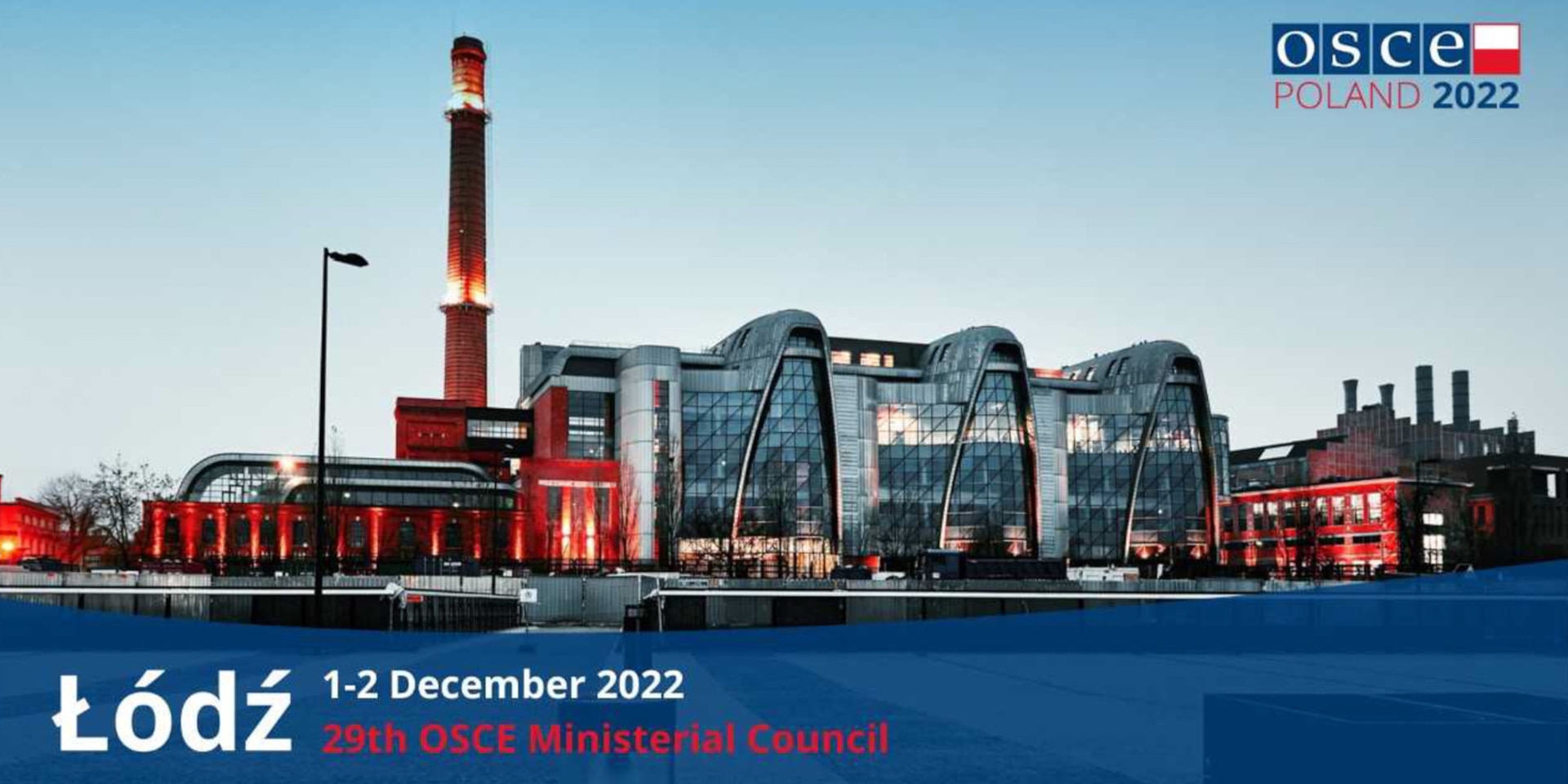 Un grand bâtiment industriel utilisé aujourd'hui comme lieu de conférence. En haut à droite se trouve le logo de la présidence de l'OSCE par la Pologne en 2022.