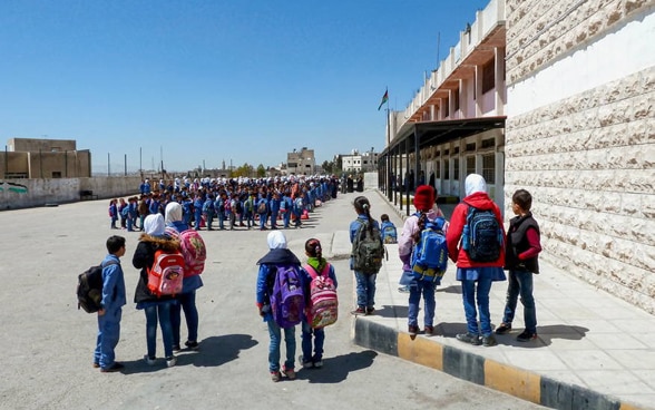 Schulkinder stehen auf dem Platz vor einer sanierten Schule in Jordanien.